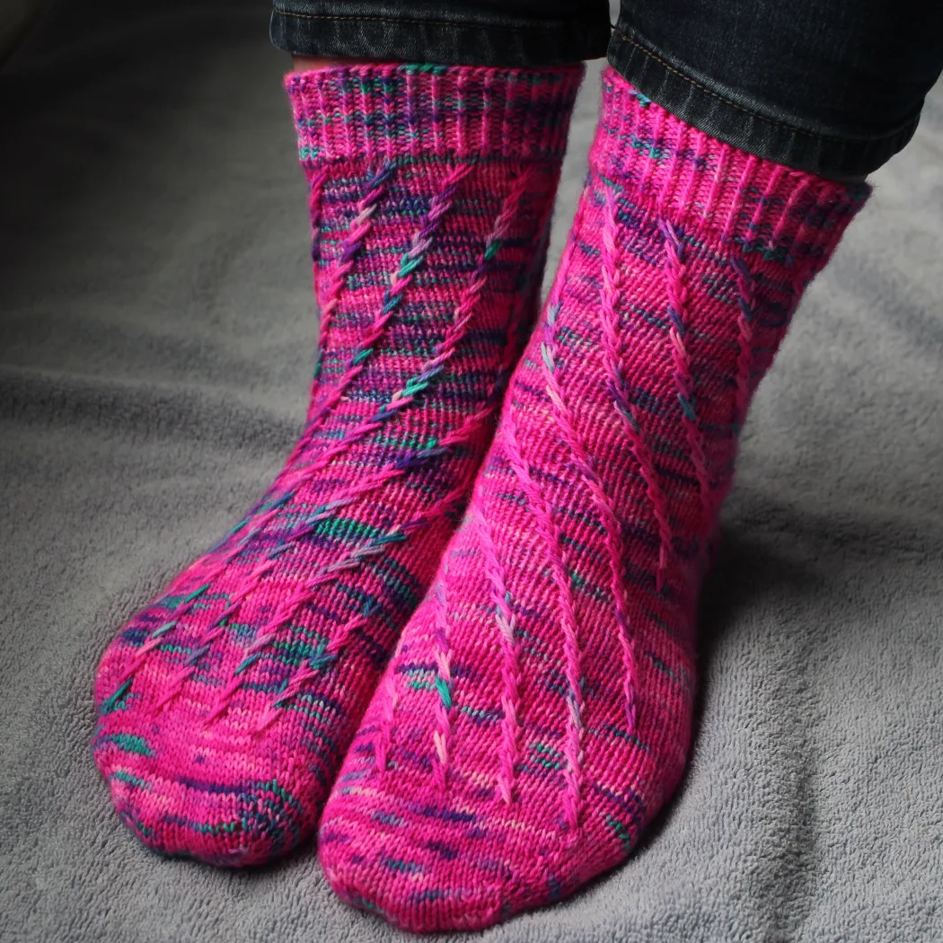 Front view of pink socks with flecks of purple and teal; they have a spiralling criss-crossing surface texture.