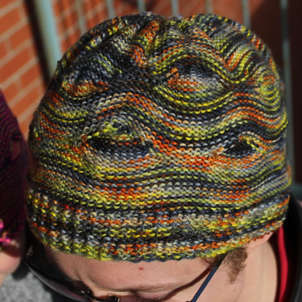 Man wearing black, green, yellow, and orange hat with large wavy textured pattern.