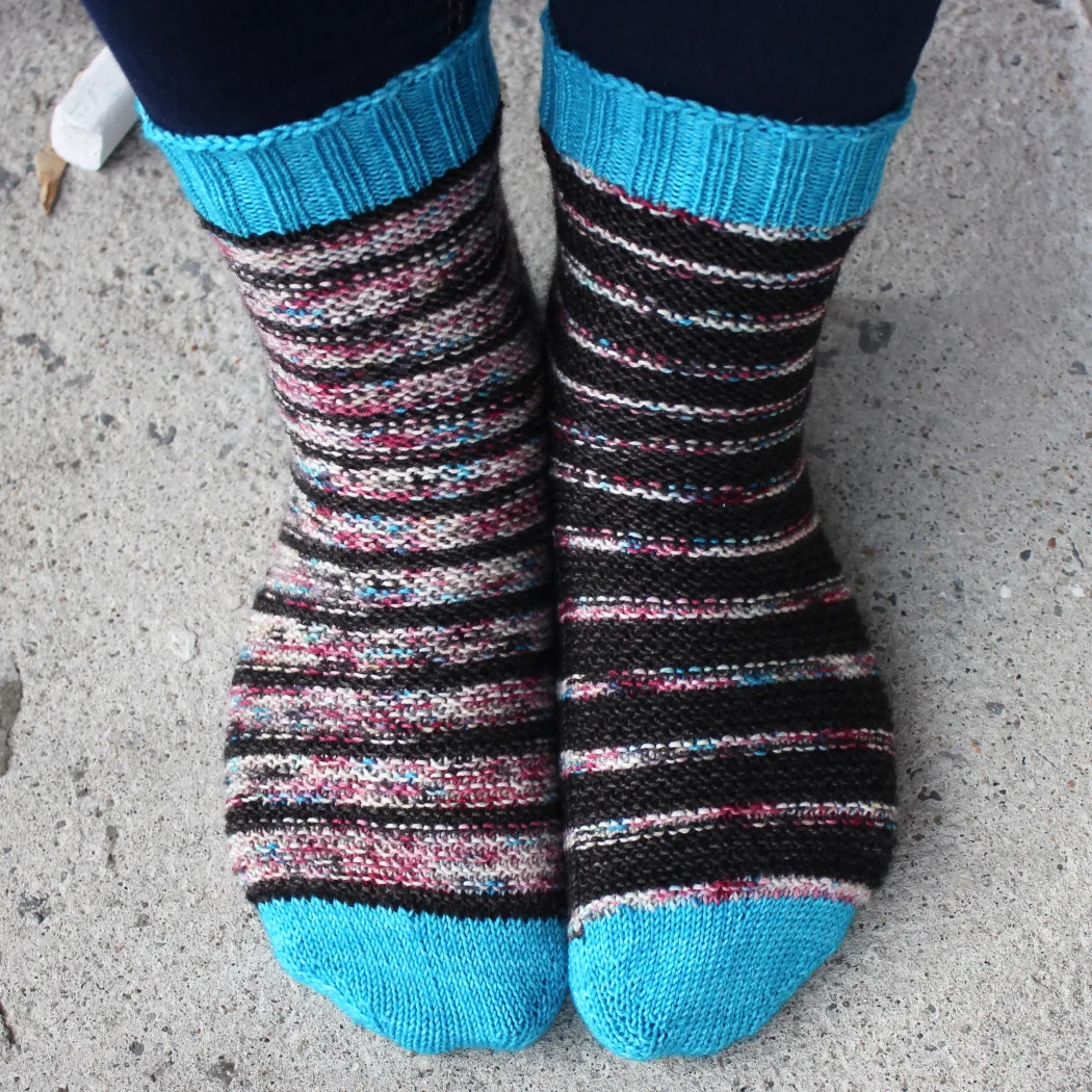 Front view of black and subtly-multicoloured striped socks with bumpy surface texture and bright blue toes and cuffs.