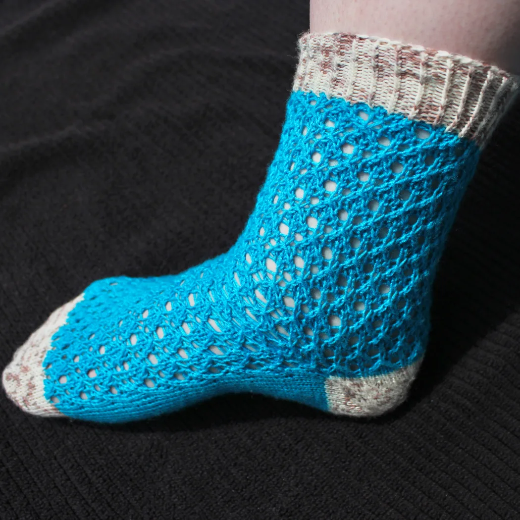 Side view of bright blue lace sock with white and brown speckled heel, toe, and cuff.