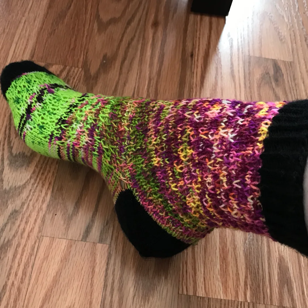 Side view of green and purple socks with a fade effect with black heel, toe, and cuff.