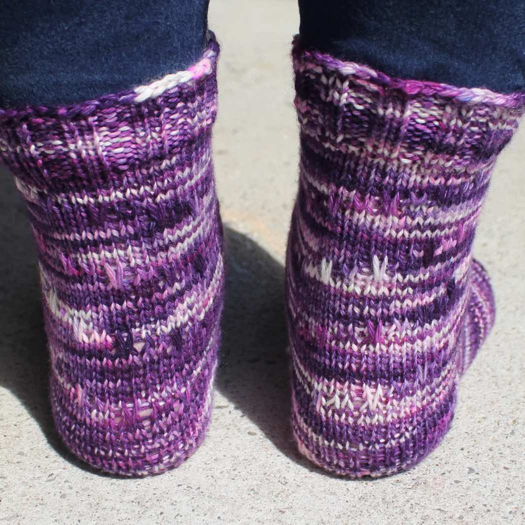 Back view of feet wearing dark purple, pink, and white socks with slipped-stitch texture.