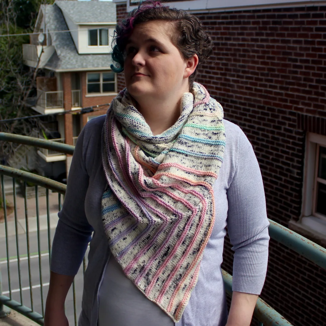 Woman wearing a thick shawl that is white with multicoloured pastel stripes wrapped around her neck.