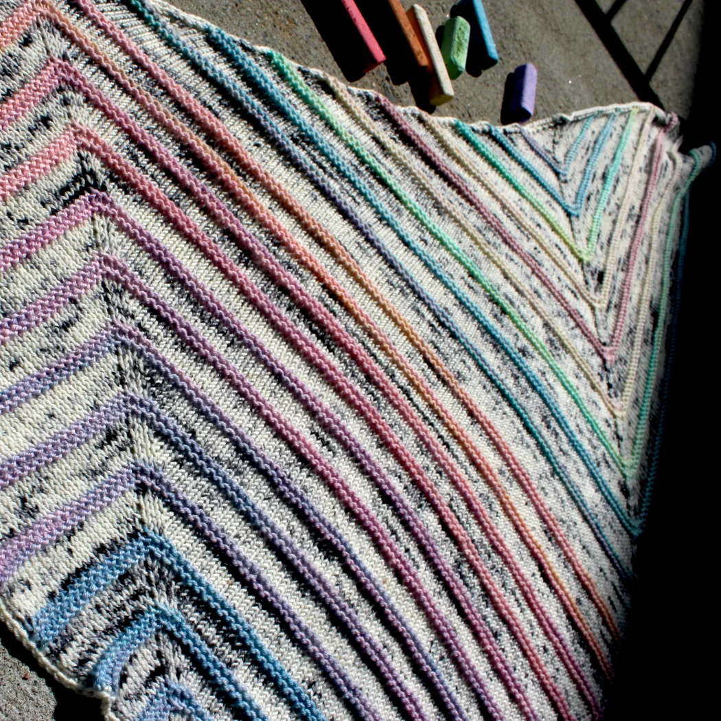 Close-up of a triangular shawl with flat white and black speckled sections between bumpy pastel stripes.