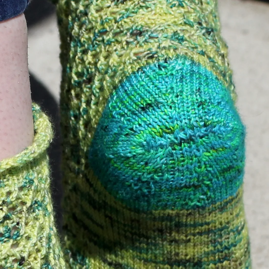 Close up view of bright blue heel on a yellow and green lace sock.