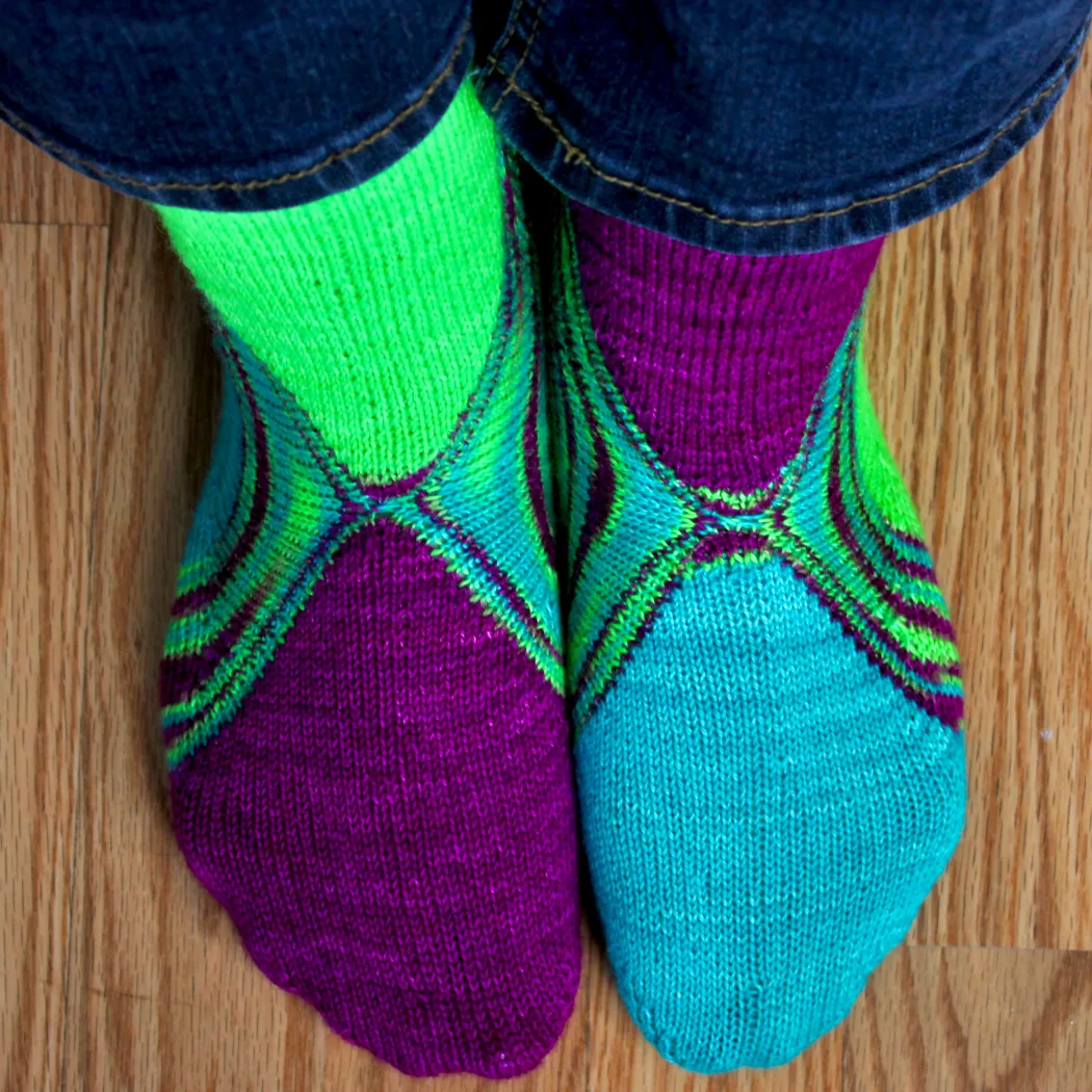 Top-down view of feet wearing bright green, blue, and purple socks with a multicoloured stripe between the colours.