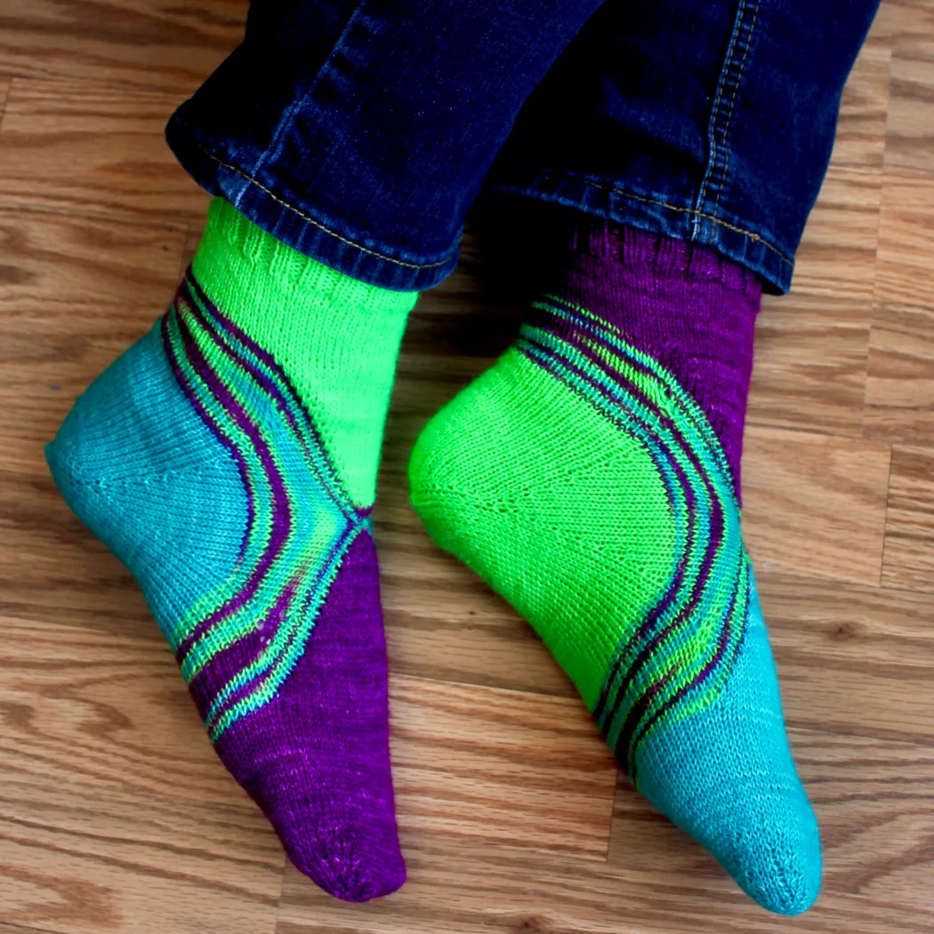 Side view of feet wearing bright green, blue, and purple socks with a multicoloured stripe between the colours.