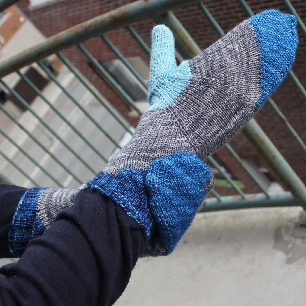 Side view of hand wearing bright yellow, blue, and orange mittens with a multicoloured stripe across the palm between the colours.