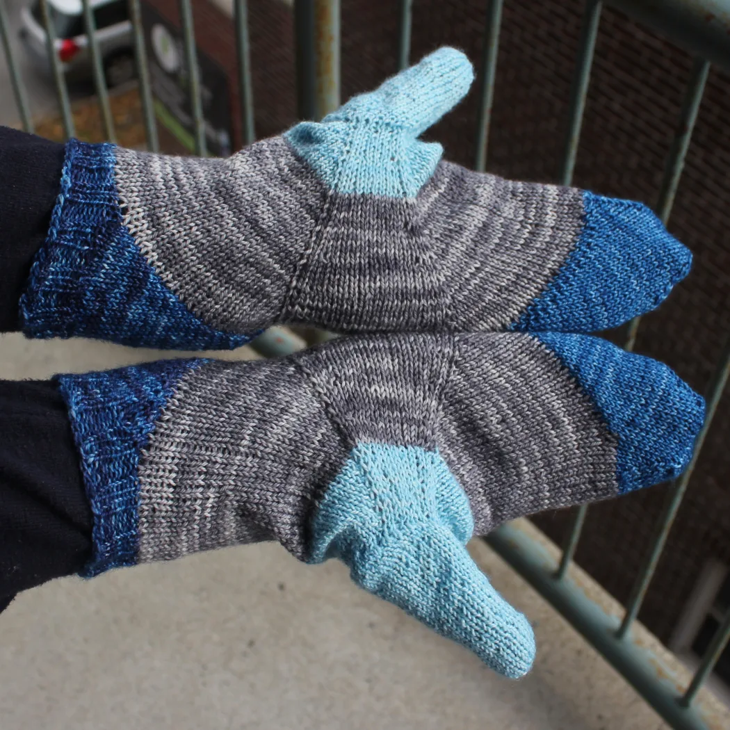 Top-down view of palms of hands wearing mittens in shades of blue with a grey stripe across the palm between the blue sections.