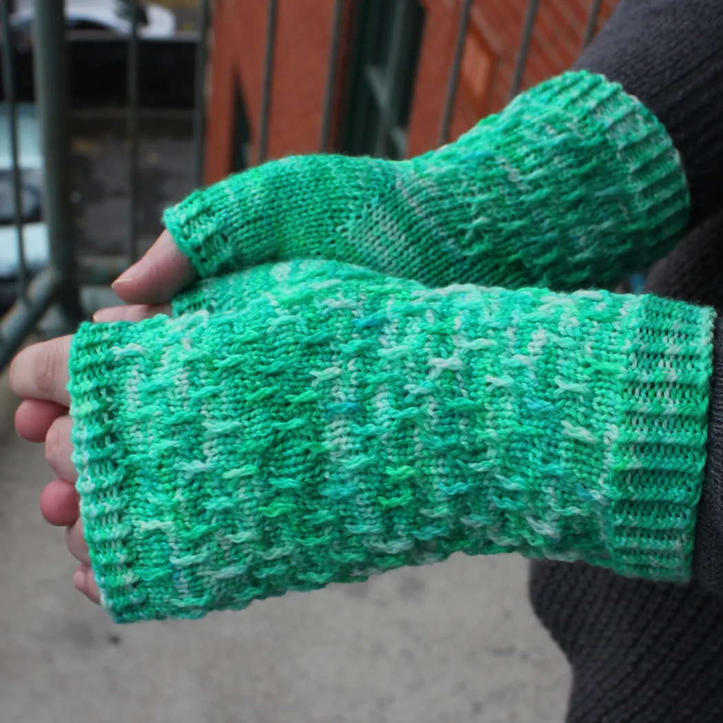 Side view of hands wearing bright green, white, and blue fingerless mitts with twisted surface detail.