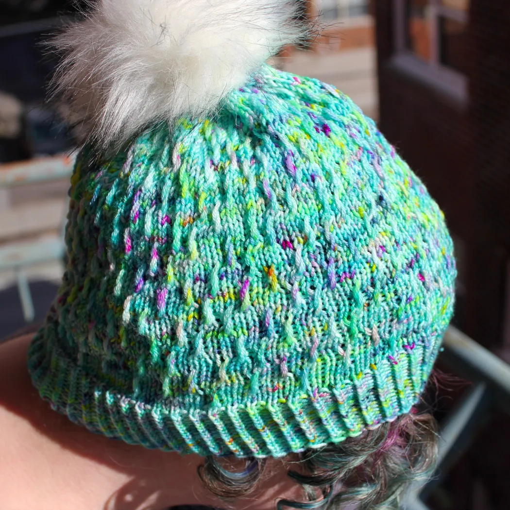 Close up of woman wearing bright green and rainbow hat with white pompom and twisted surface texture.