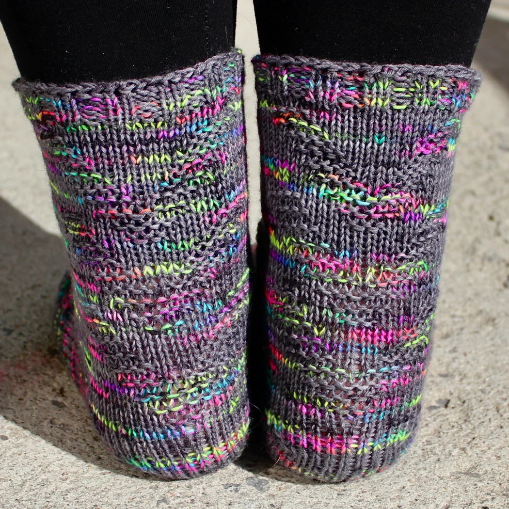 Back view of feet wearing dark grey and rainbow socks with raised chevron texture.