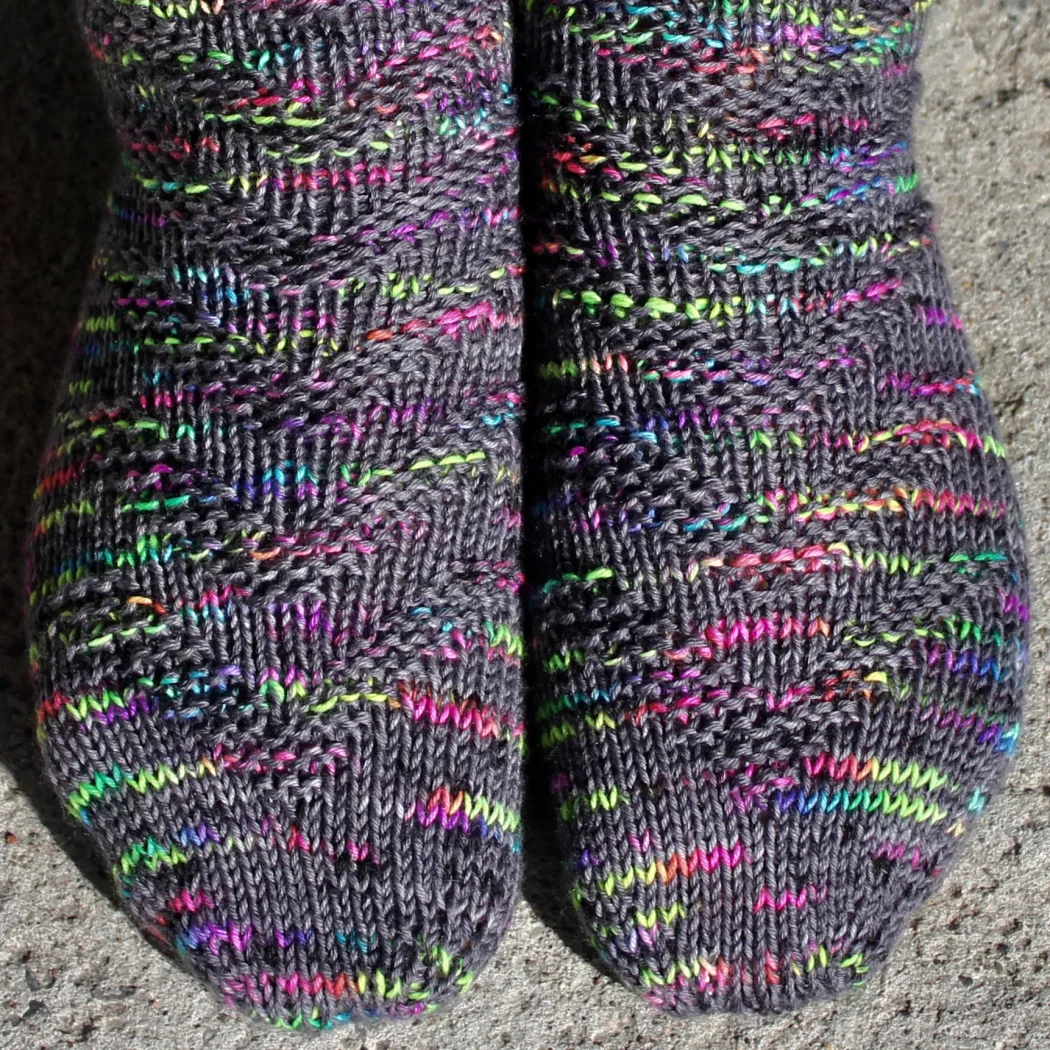 Close up of feet wearing dark grey and rainbow socks with raised chevron texture.