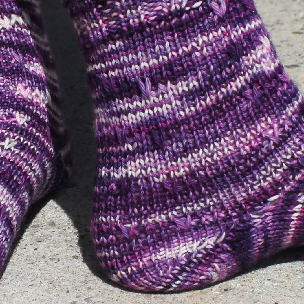 Close up of side and heel of dark purple, pink, and white socks with slipped-stitch texture.