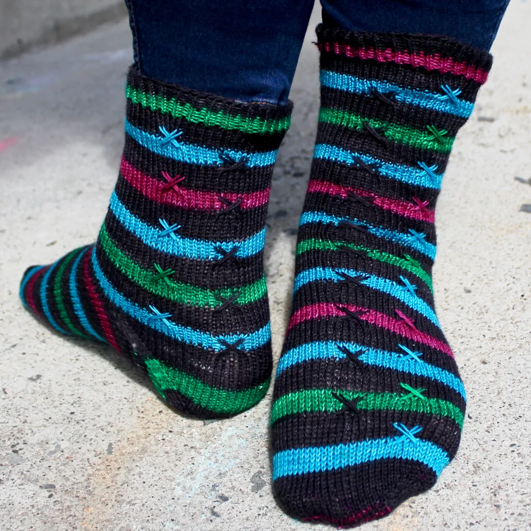 Feet turned so one is frontwards and one is backwards, wearing striped knitted socks with X stitch details on top of the stripes.