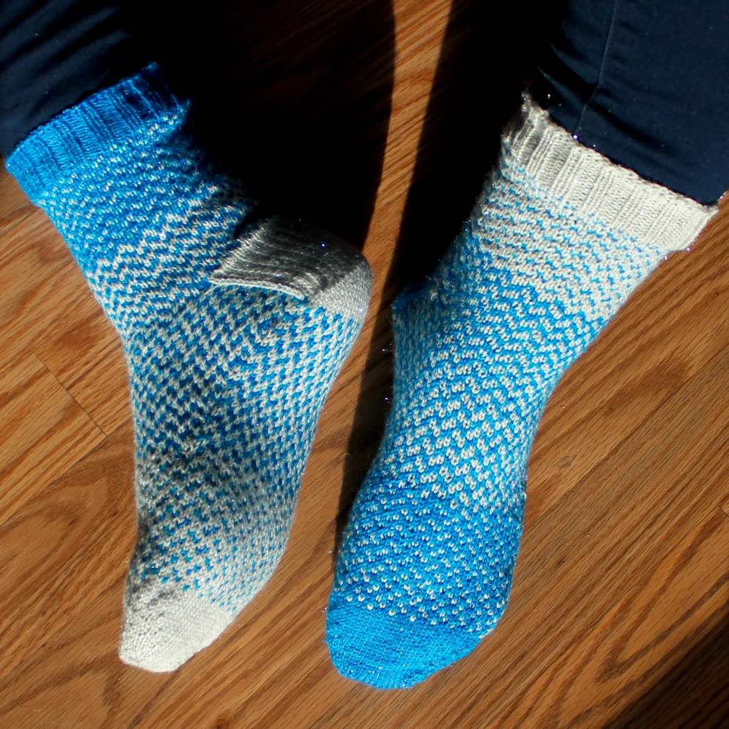 Blue and white sparkly colourwork socks shown on one foot from above and on the other from the side and sole.