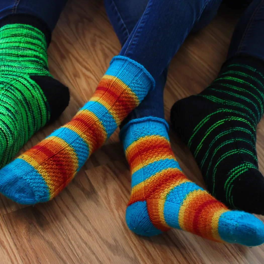 Crossed child feet wearing striped socks with texture detail and blue heels between adult feet wearing matching green and black socks with black heels.