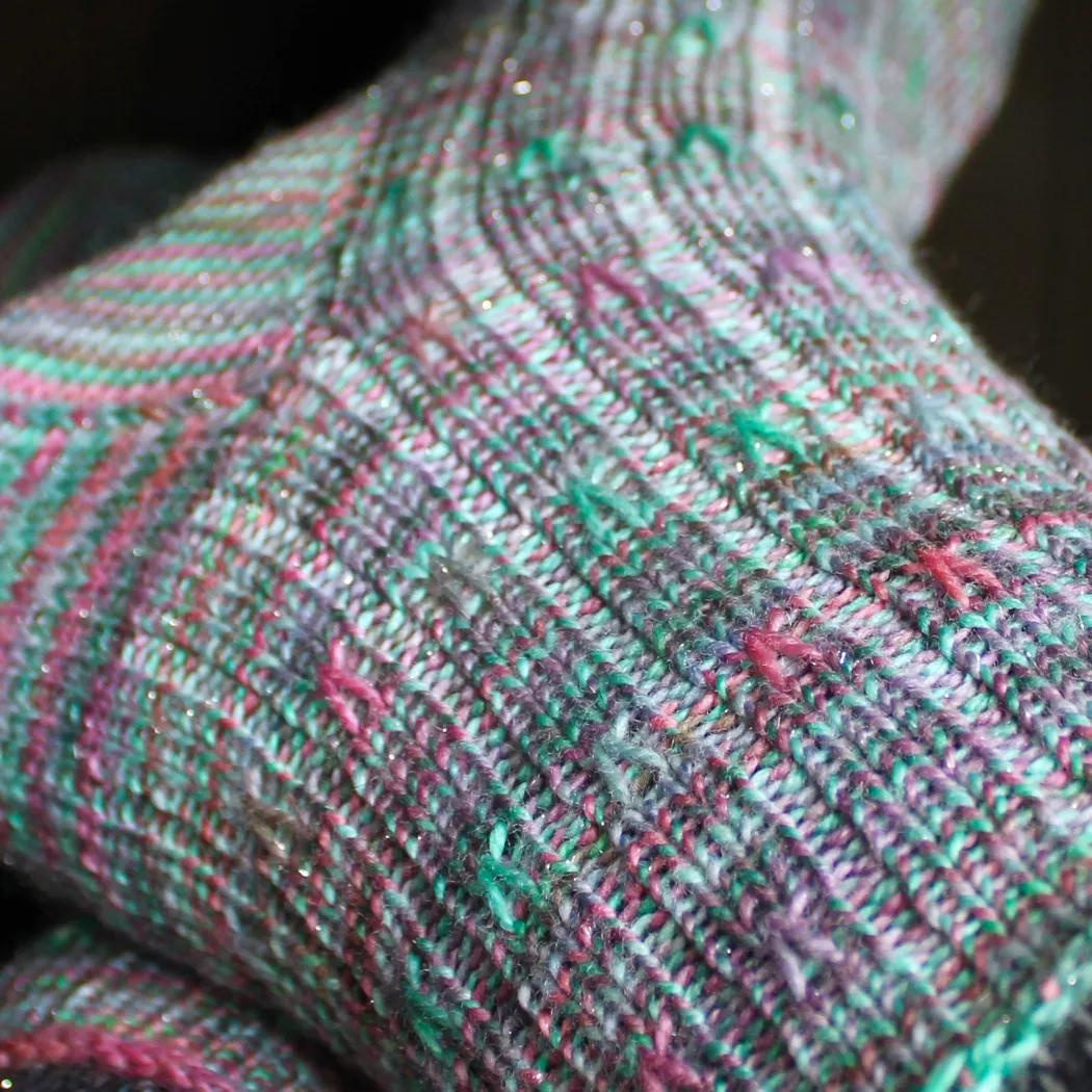 Close up of green ribbed socks with coral and purple spiralling surface detail.