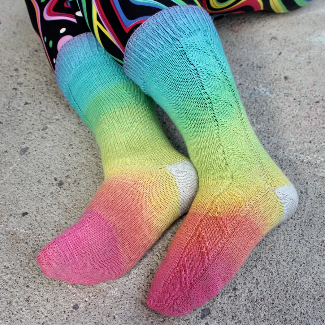 Side view of feet wearing rainbow socks with diagonal slipped-stitch panel and sparkly white heels.