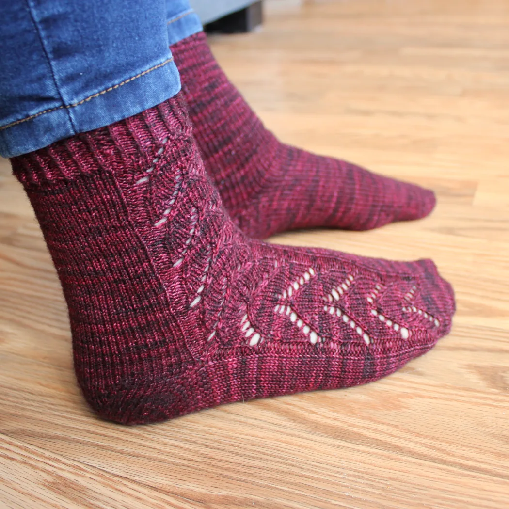 Side view of feet wearing red socks with lace panel of interlocking hearts.