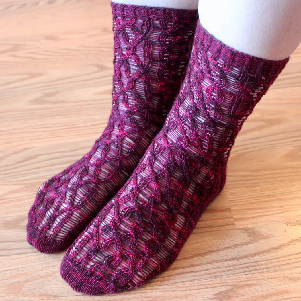 Feet wearing red cabled socks with beads on strands between the cable crosses.