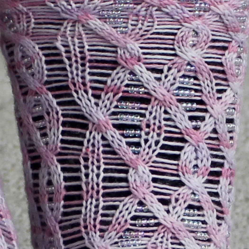 Close up of light pink cabled socks with beads on strands between the cable crosses.