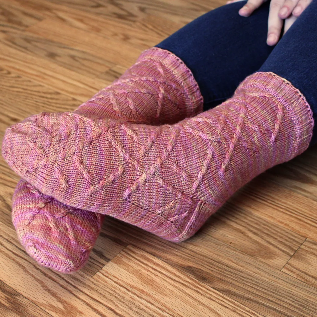 Slightly crossed feet wearing pink-orange socks with cabled surface detail.