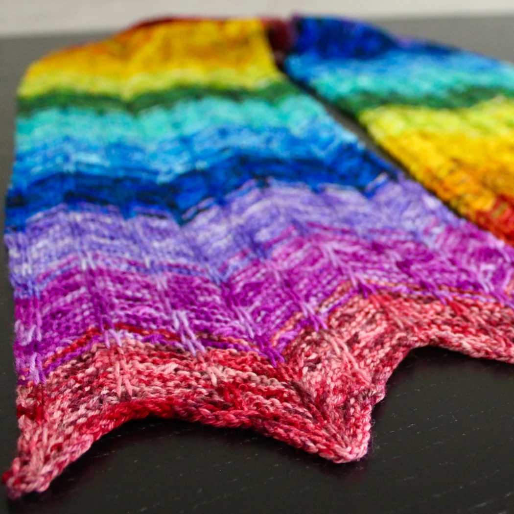 Bright rainbow textured scarf with zigzag edge laid flat on a table.