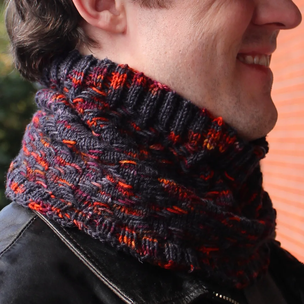 Man wearing cowl that is black with bright orange and burgundy highlights in a zigzag texture.