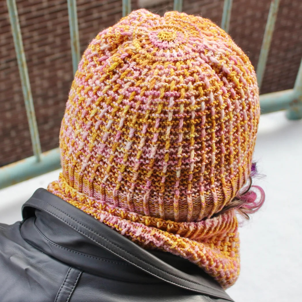 Back view of woman wearing yellow and pink hat with circular patterned crown and twisted and ridged surface texture.