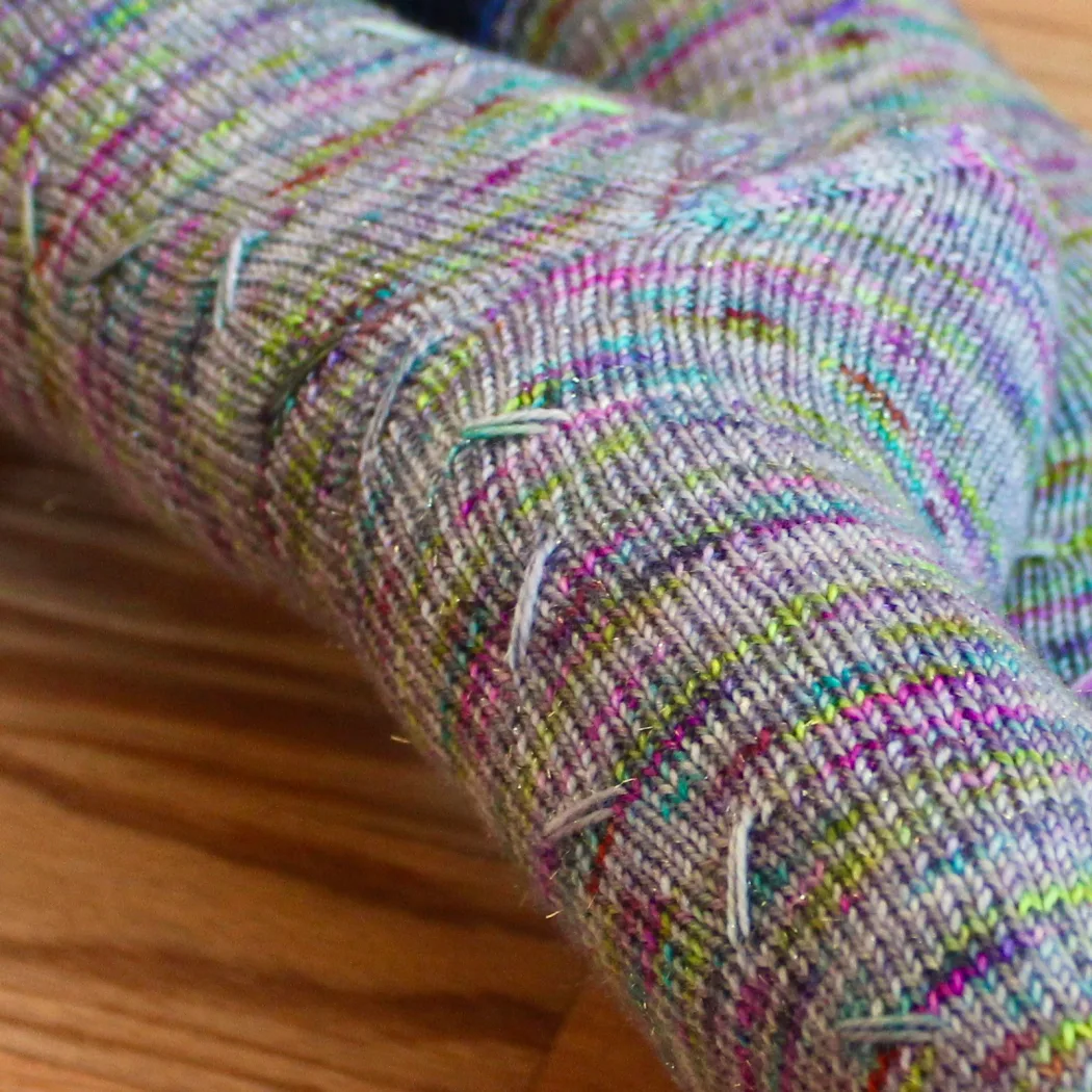 Close up of grey socks with rainbow speckles that have lines of diagonal elongated stitches.