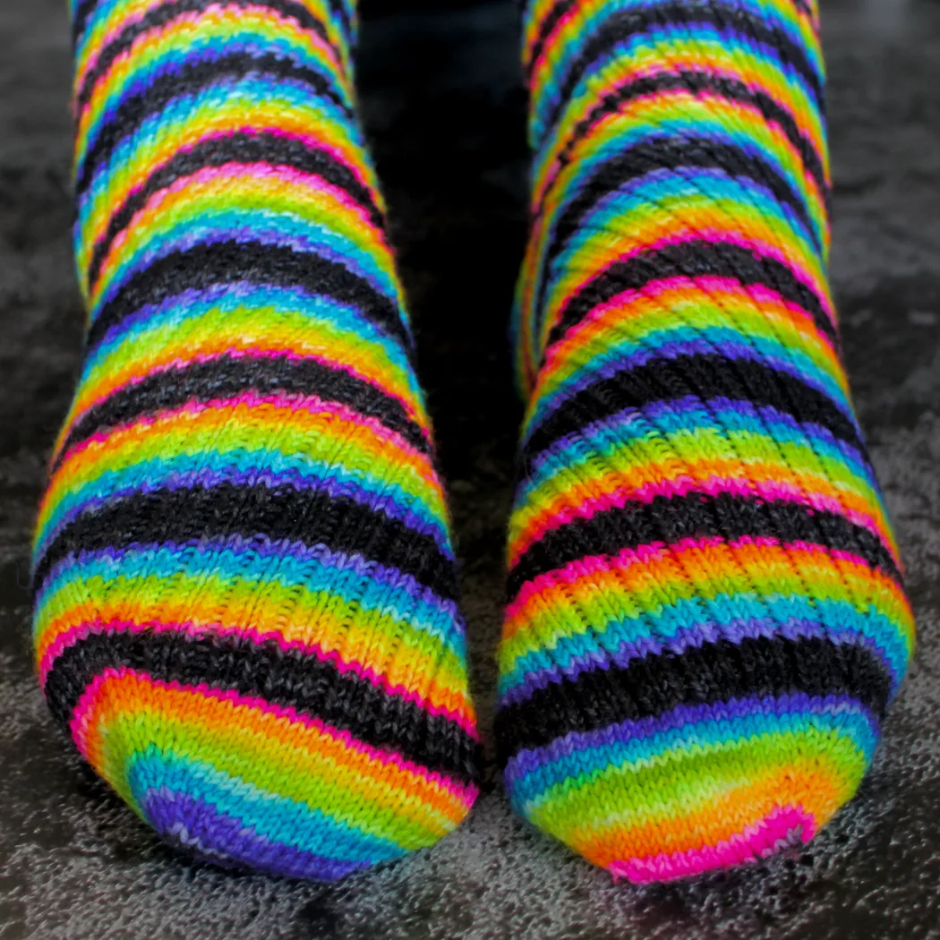 Close up of toes and feet wearing black and rainbow striped socks with mirrored diagonal ribbing.