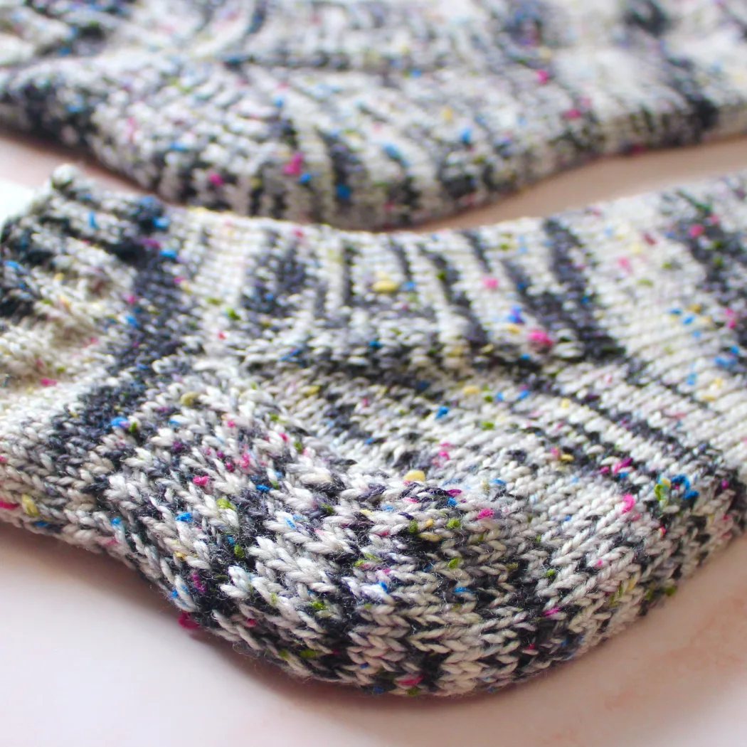 Close up of heel and gusset of one black and white heavyweight socks with rainbow flecks lying flat.