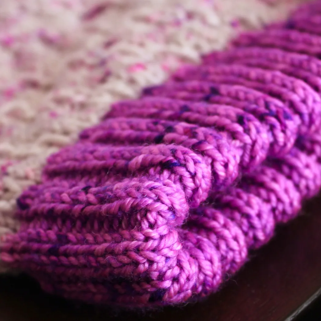 Close-up of thick, neon purple ribbed cuff of knitted hat on a flat surface.