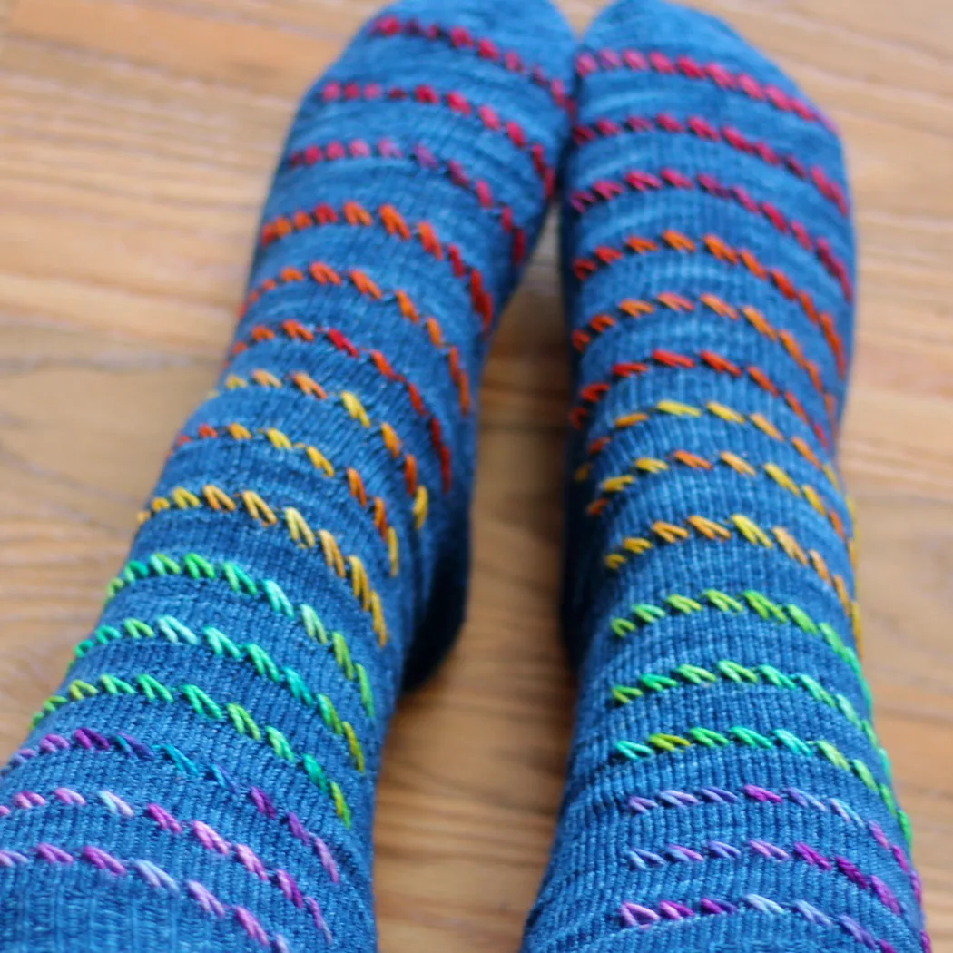 Wide view of tall blue socks with rainbow diagonal surface texture.