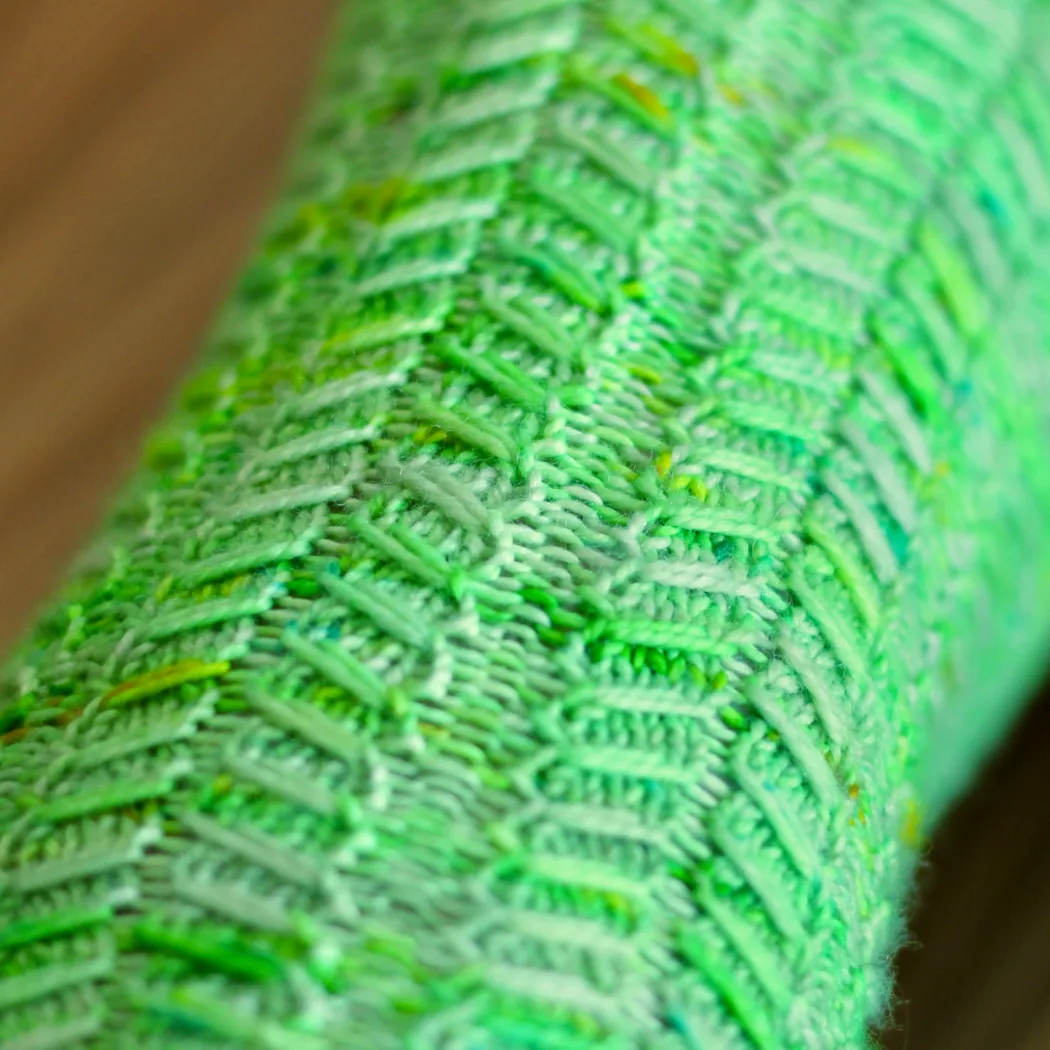 Close up of green knitted socks with mirrored slipped-stitch cable texture.