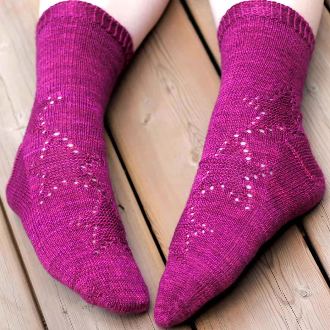 Feet wearing dark pink knitted socks with spiralling star motif in texture and eyelets.