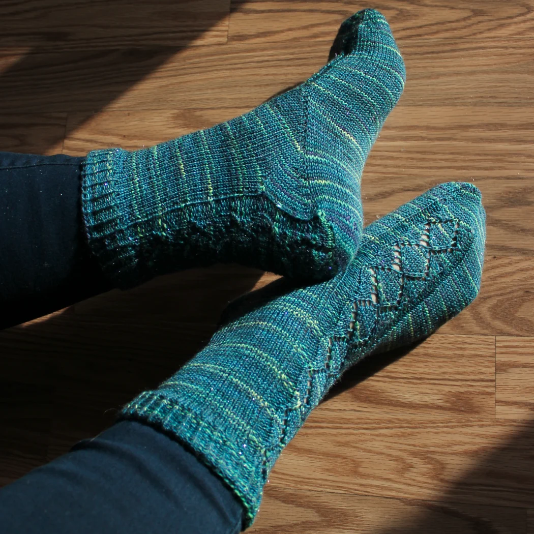 Close up of feet wearing blue socks with lace panel that runs diagonally across the foot; a second panel is visible on the back of the leg.