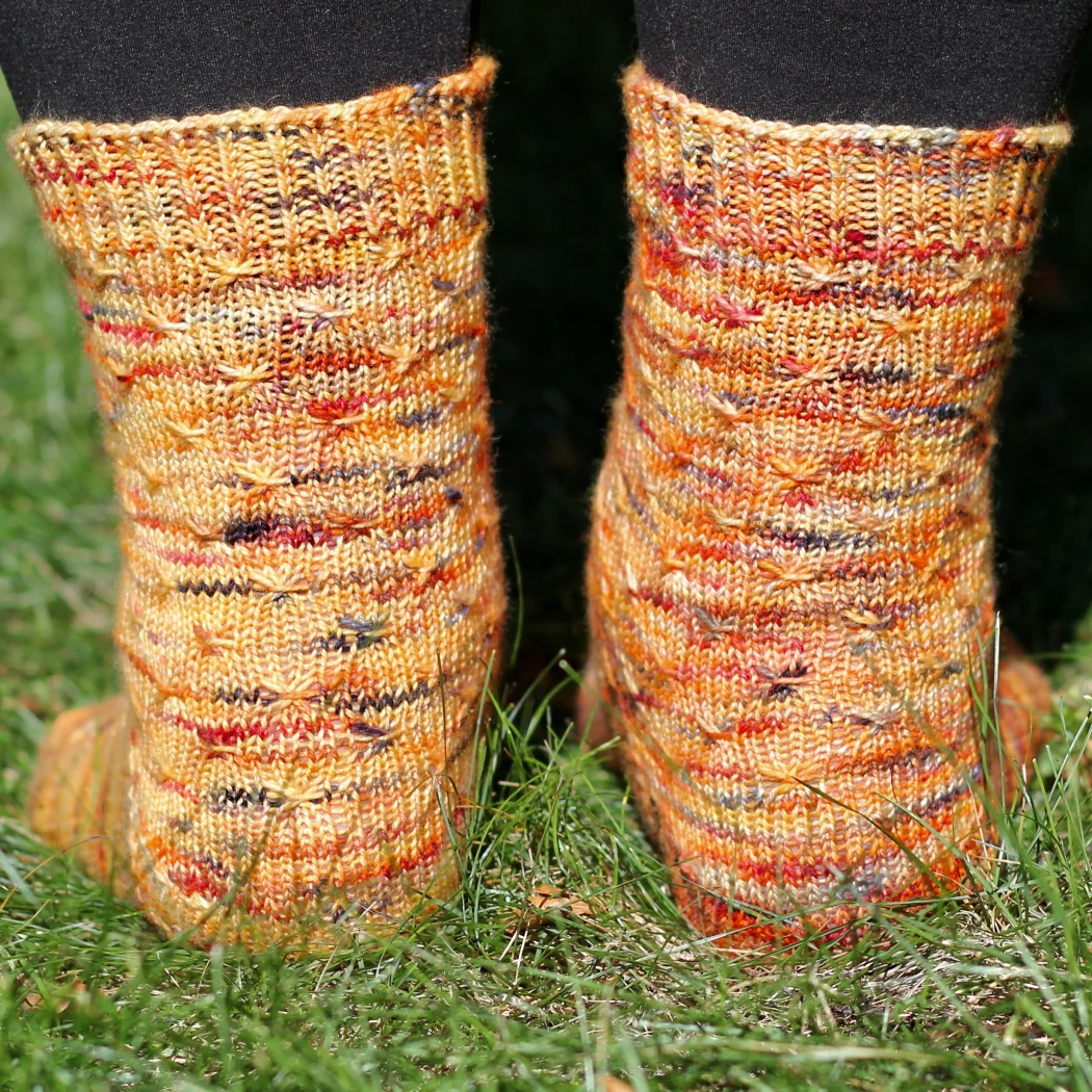 Back view of orange socks with asterix-like cable texture.