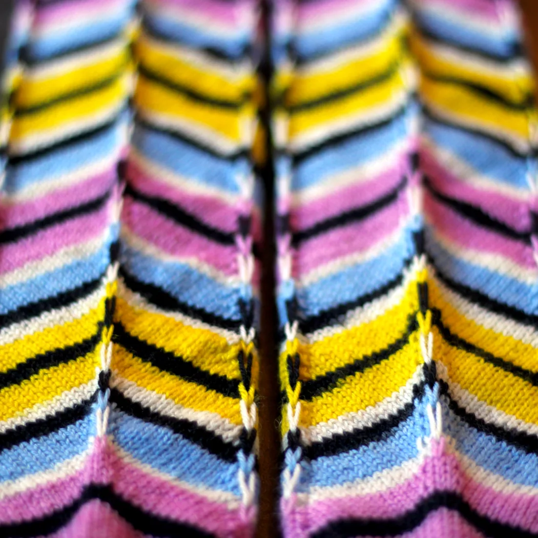 Close up of side-by-side matching striped knitted socks on sock blockers with graphic distorted diagonal pattern.