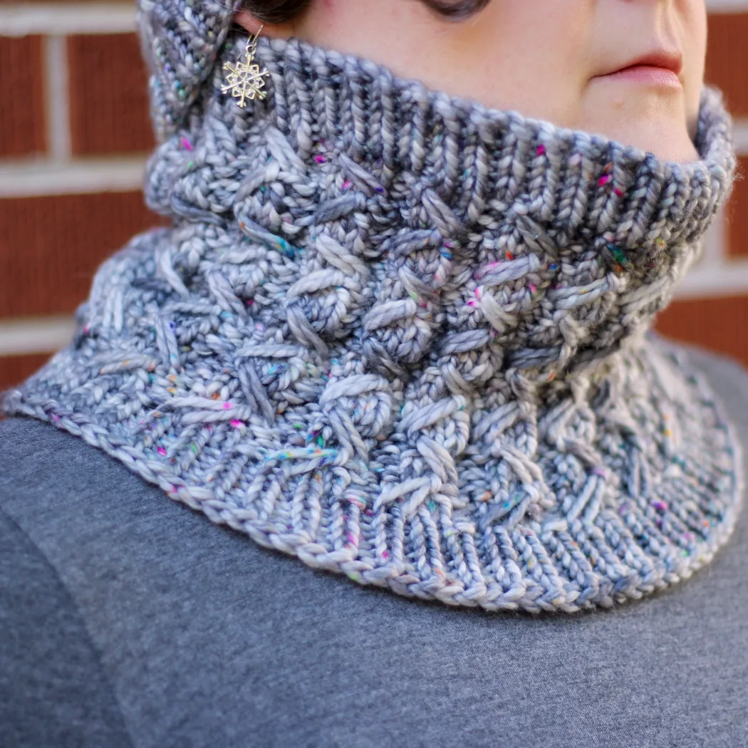 Woman wearing grey knitted cowl with textured ribbing.