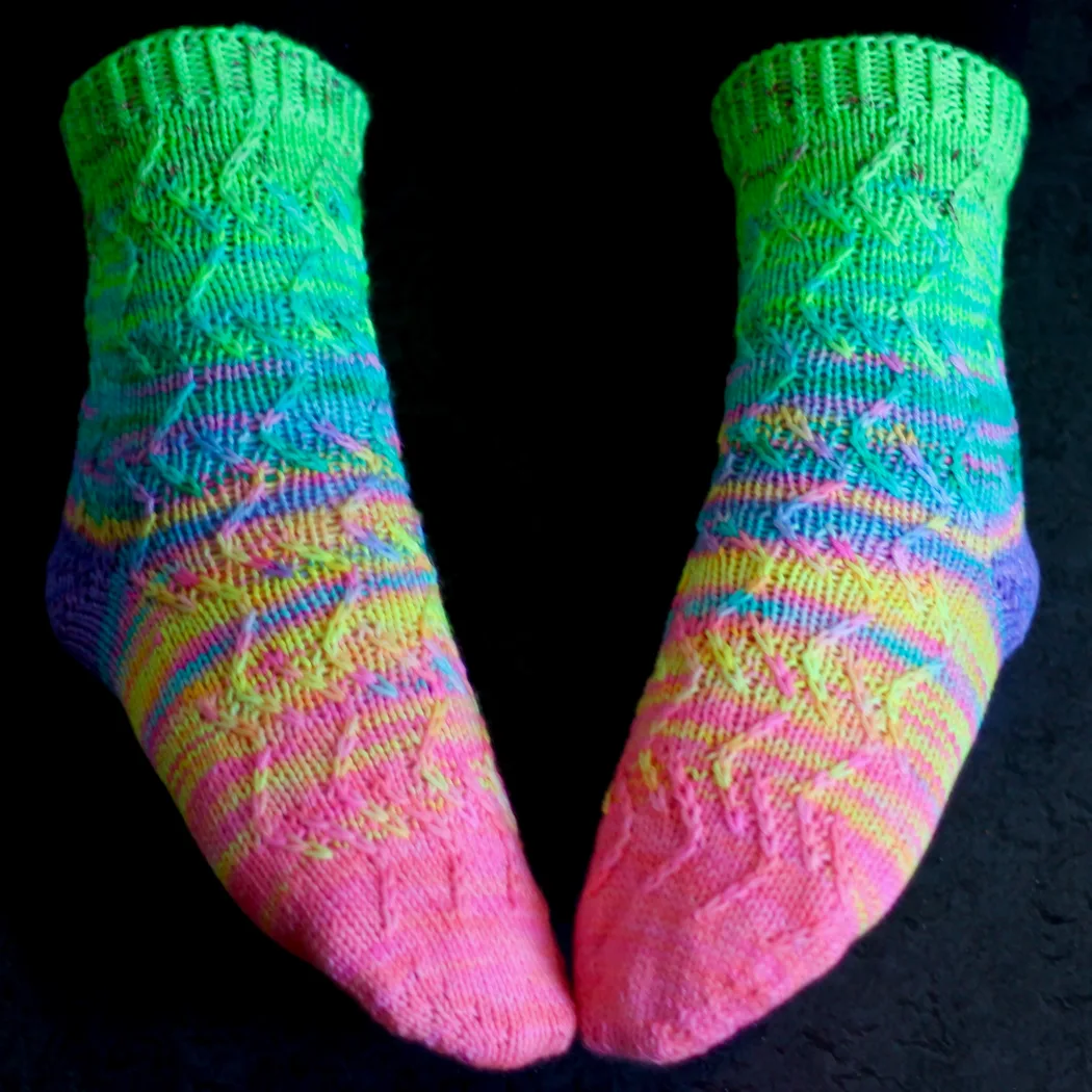 Feet wearing neon rainbow knitted socks with zigzag surface texture.