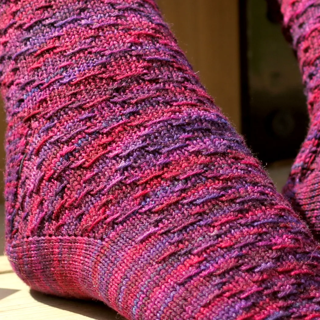 Close up of foot wearing red and purple sock with horizontal diamond-shaped surface texture.