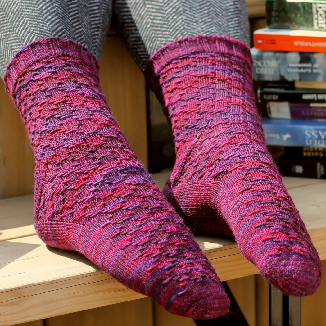 Feet wearing red and purple socks with horizontal diamond-shaped surface texture with novels in the background.