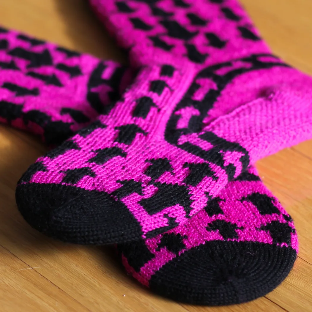 Black and pink stranded colourwork socks on sock blockers with arrow motifs pointing down on the leg, up on the foot, and around the ankle.