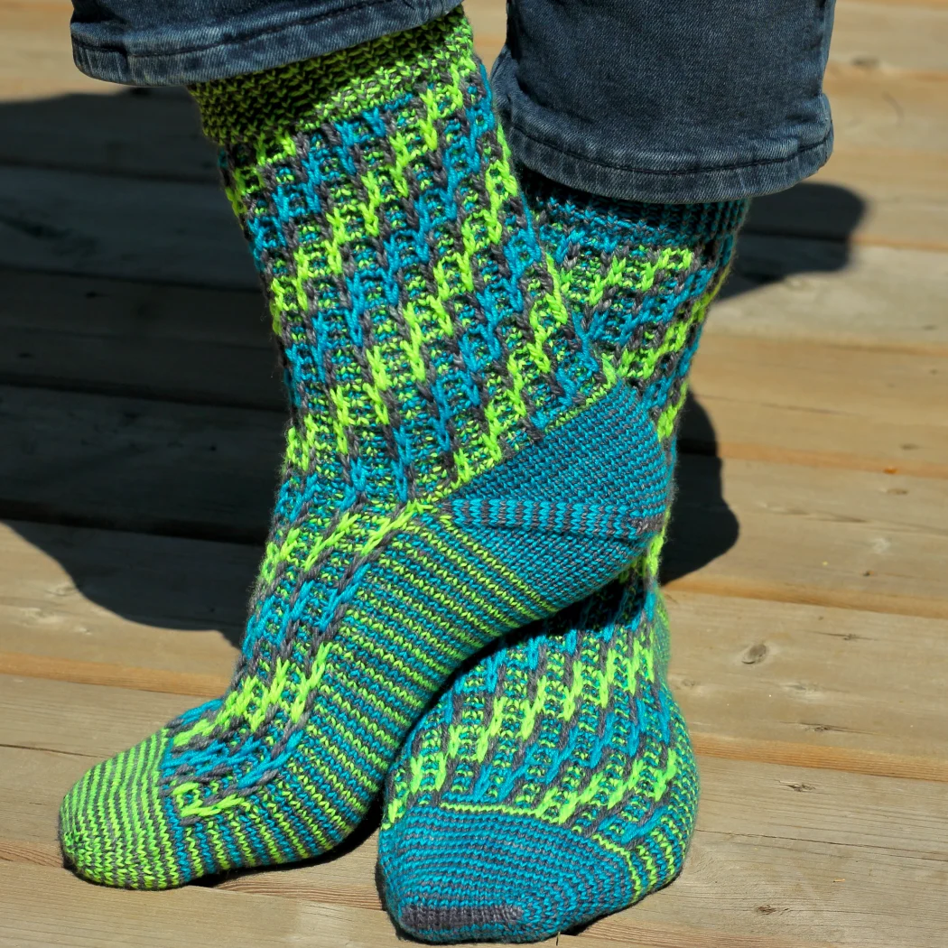 Feet wearing grey, blue, and neon green knitted socks with spiralling ladder motif.