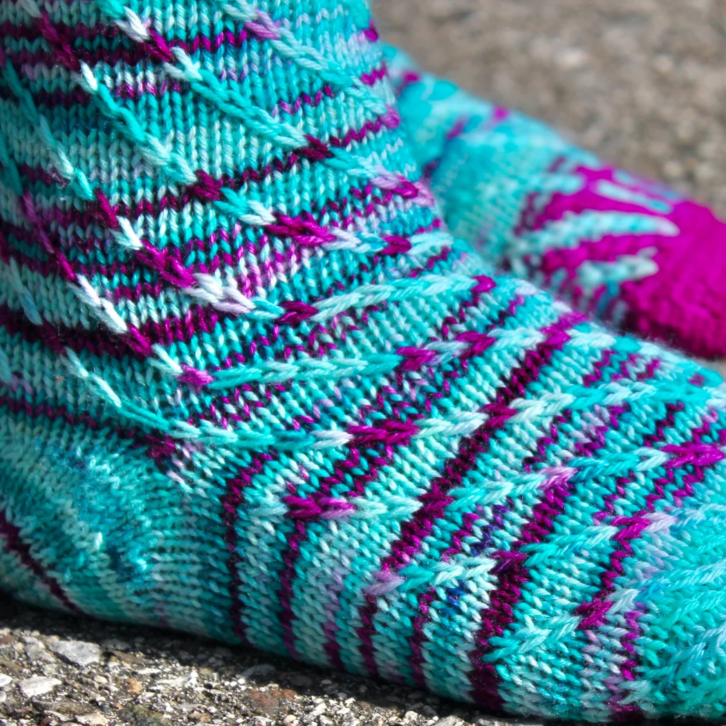 Close up of feet wearing turquoise and magenta knitted socks with spiralling slipped-stitch texture.