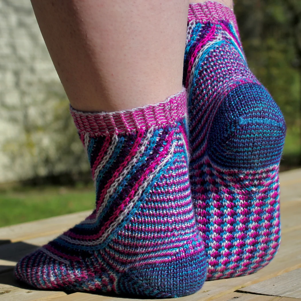 Back view of feet wearing knitted socks in four colours with slipped stitch motifs and mini-gusset shaping.