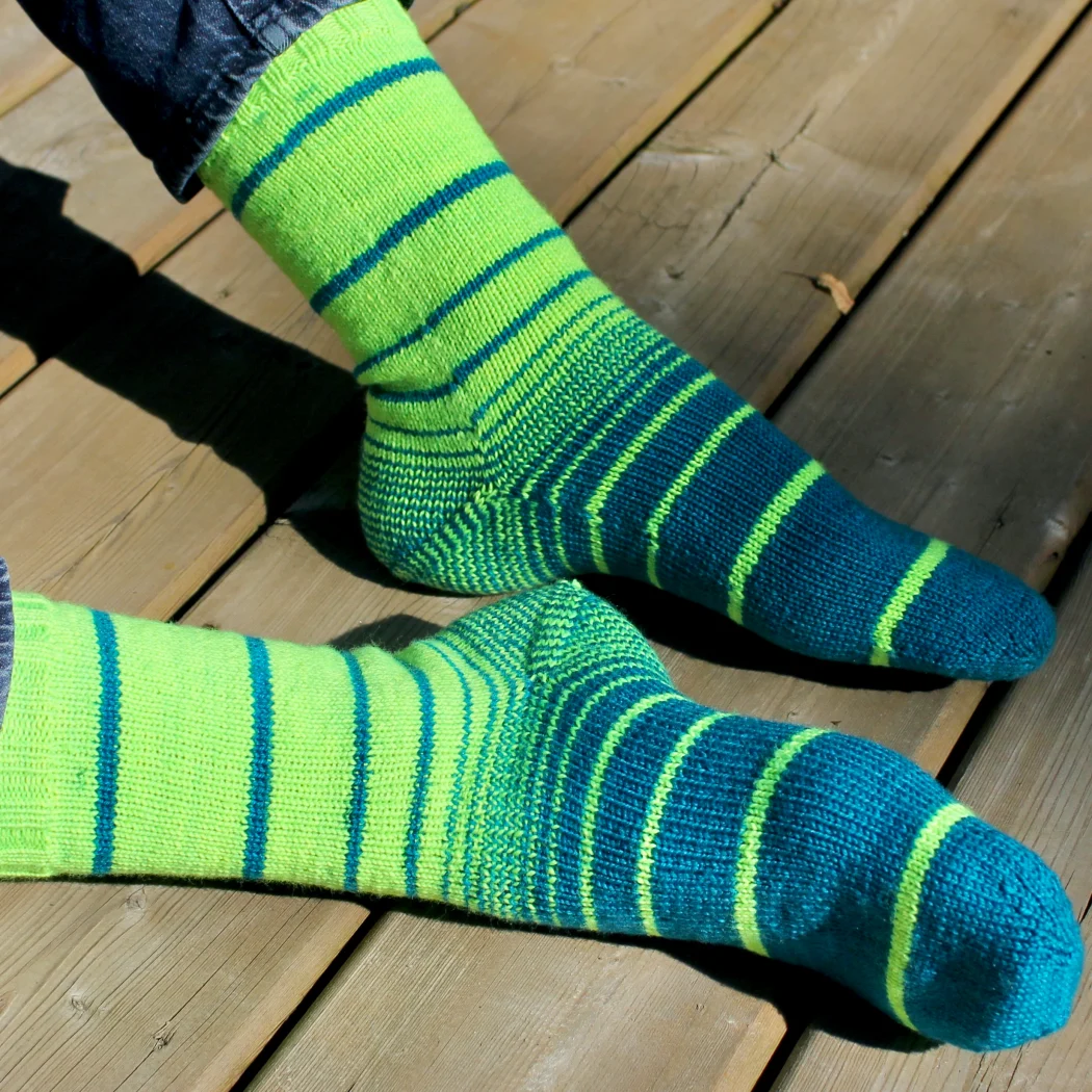 Feet wearing bright green and teal knitted socks in a variable-width striping pattern with striped heels.