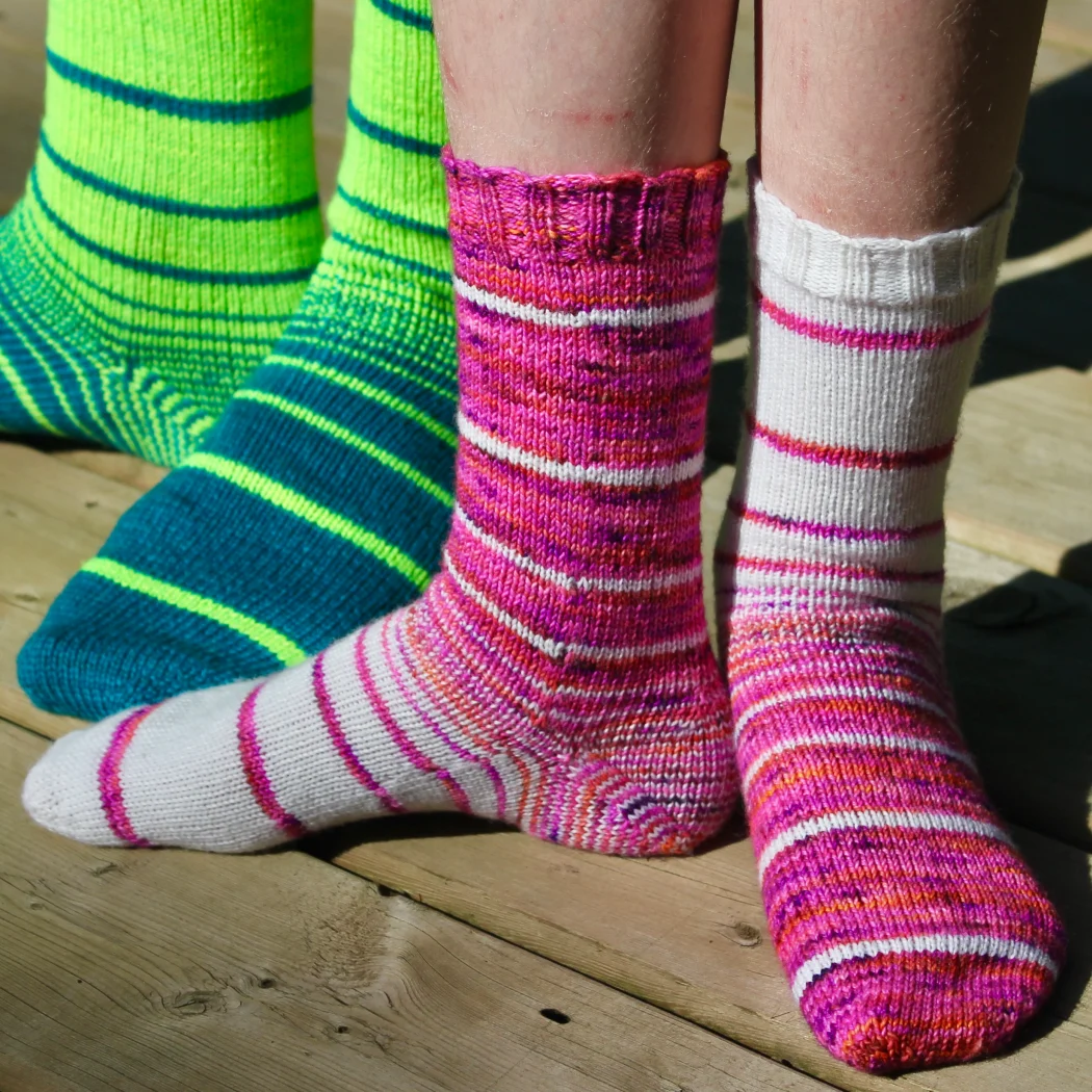 Two pairs of feet wearing knitted socks in a variable-width striping pattern with striped heels.